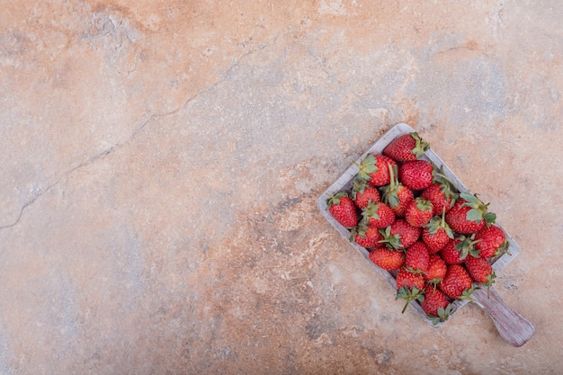 Red strawberries in a rustic wooden platter on the marble