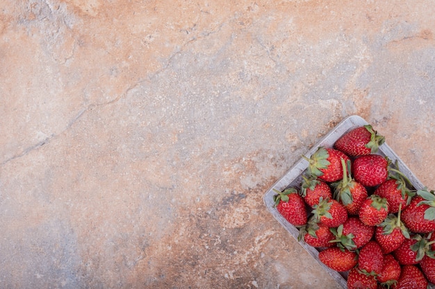 Red strawberries on square rustic platter.