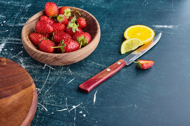 Red strawberries in a wooden cup with lemon slices aside. 