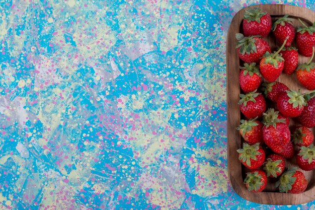 Red strawberries in a wooden platter on blue background