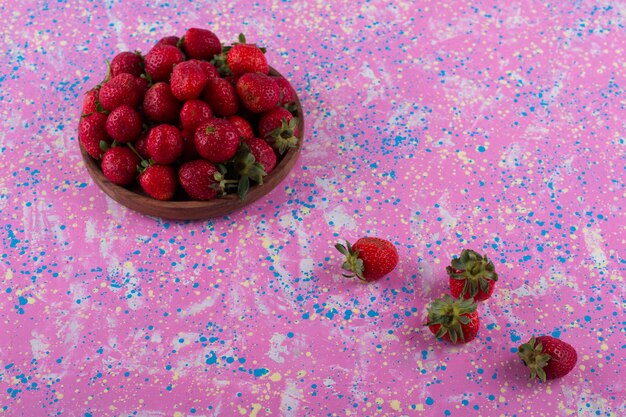 Free photo red strawberries in a wooden platter and on the table