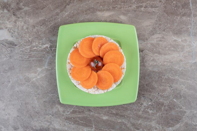 Red tomato in the middle of the carrot slices, and rice cake underneath on the plate , on the marble surface