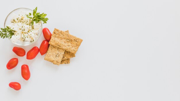 Red tomatoes and crisp bread with cheese bowl on white background