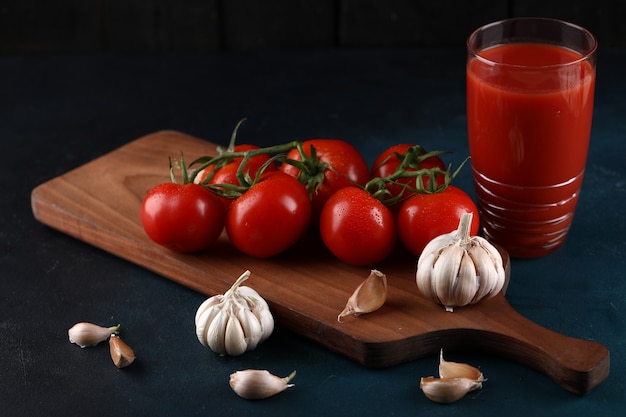 Pomodori rossi, guanti all'aglio e un bicchiere di succo di pomodoro su sfondo blu.