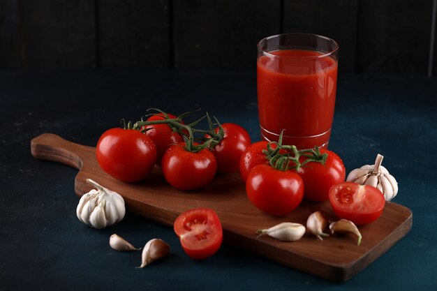 Red tomatoes and garlic gloves on the wooden board with a glass of juice.