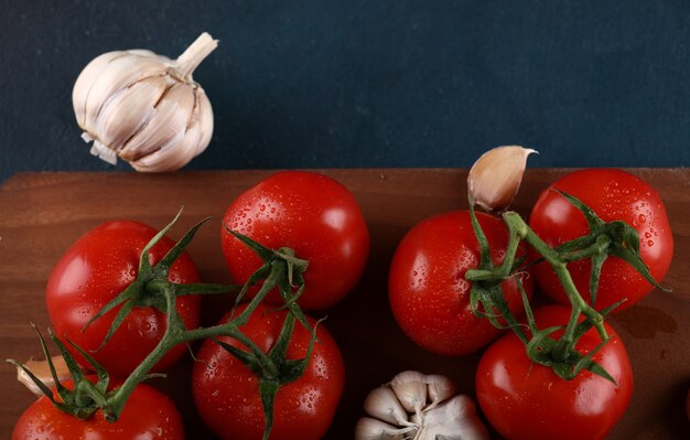 Red tomatoes and garlics on a wooden board on blue background.