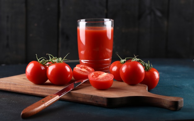Red tomatoes and a glass of juice on a wooden board.
