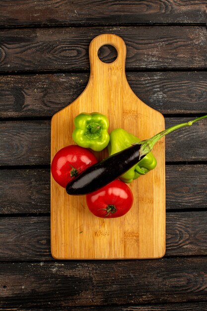 Red tomatoes a top view of fresh ripe vegetables such as green bell peppers and eggplant on a yellow-brown desk on a wooden brown rustic floor