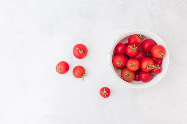 Red tomatoes in white bowl on white textured background