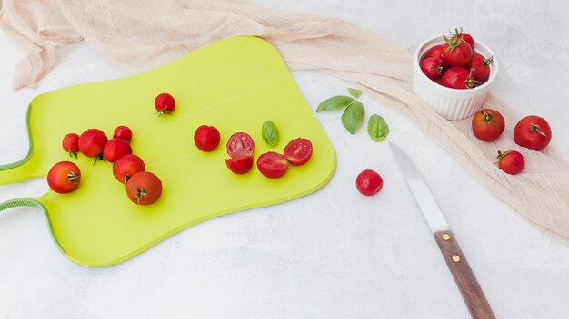 Red tomatoes with basil on chopping board with knife and scarf on white backdrop