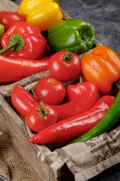 Red tomatoes with peppers in a wooden tray.