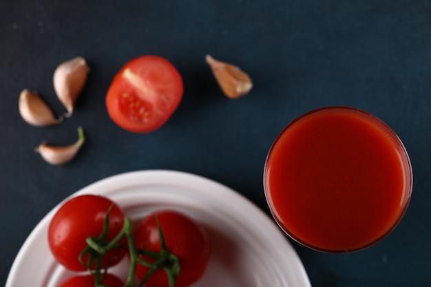 Free photo red tomatoes with water sprinkles on them in a white plate with a glass of juice. top view.