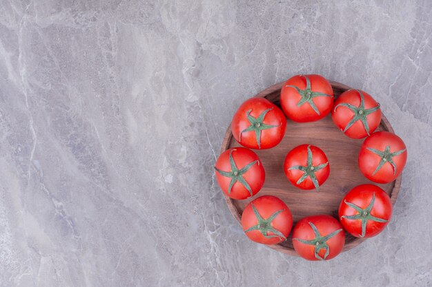 Red tomatoes in a wooden platter on marble.