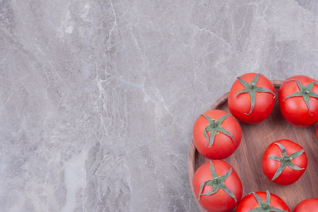 Free photo red tomatoes in a wooden platter on marble.