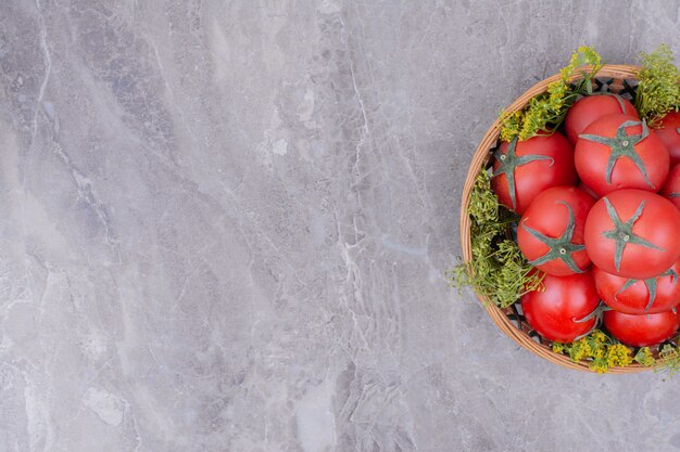 Red tomatoes in a wooden platter on marble.