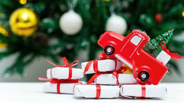 その上にクリスマスツリーと下にたくさんの贈り物が付いている赤いおもちゃの車。背景のクリスマスツリー