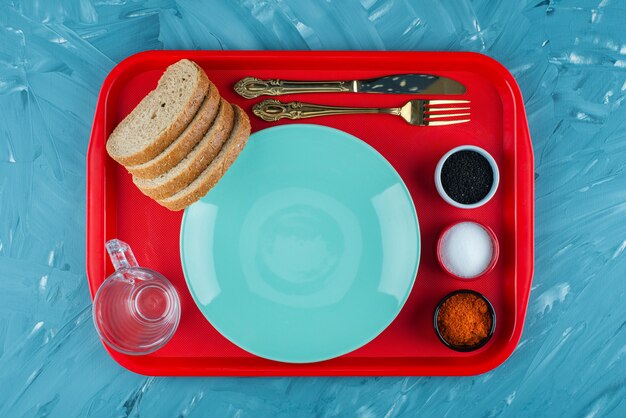 A red tray of an empty blue plate with sliced brown bread and spices . 