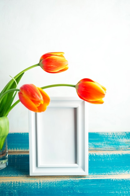 Free photo red tulips in glass vase with blank frame