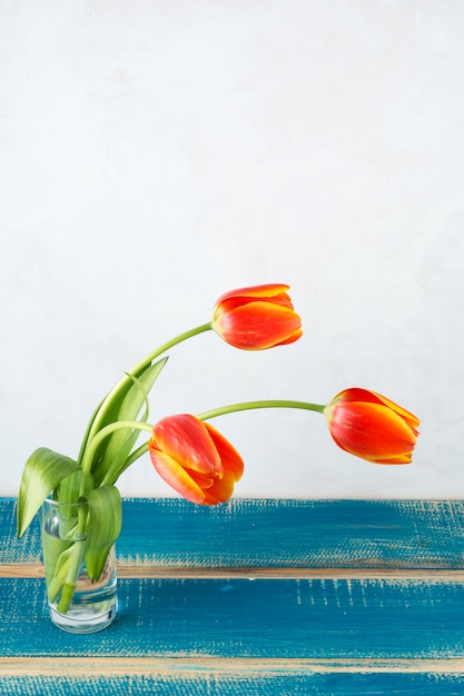 Free photo red tulips in glass vase on wooden table