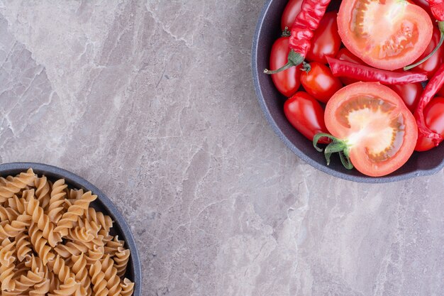Red uncooked pastas with cherry tomatoes on the marble surface