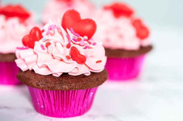 Красные бархатные кексы с розовой итальянской масляной глазурью и украшены красными шоколадными конфетами в форме сердца и поцелуев.