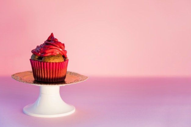 ピンクの背景に対してcakestandのカップケーキの上の赤いホイップクリーム