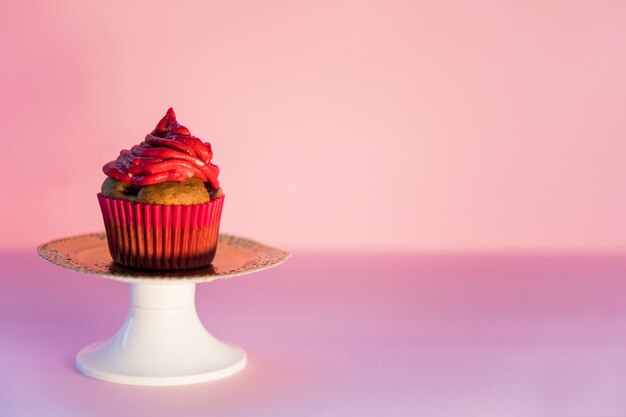 Red whipped cream over the cupcake on cakestand against pink backdrop