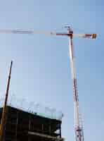 Free photo red and white construction crane in front of building against blue sky