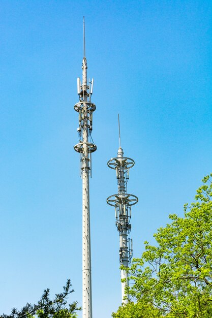 Red and white tower of communications with a lot of different antennas under blue sky and clouds