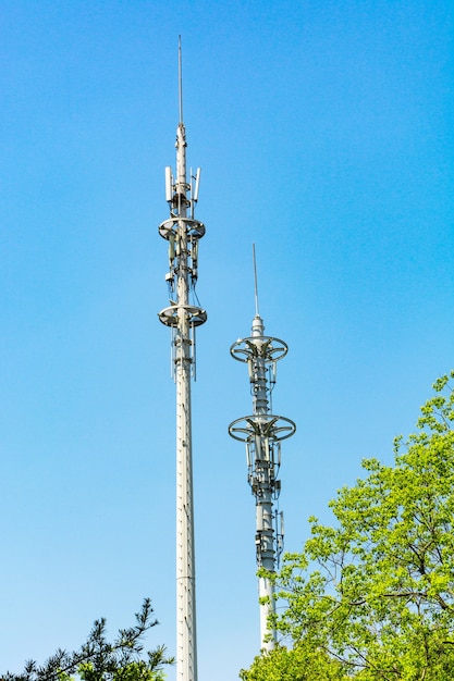 Red and white tower of communications with a lot of different antennas under blue sky and clouds