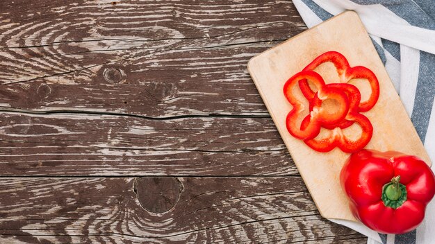 Red whole and slices of bell pepper on chopping board over the wooden desk