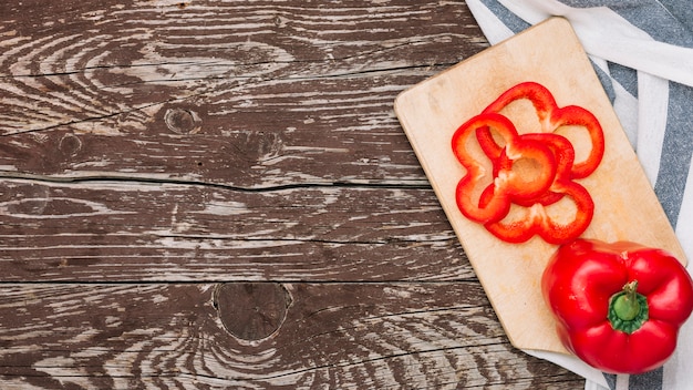 Red whole and slices of bell pepper on chopping board over the wooden desk