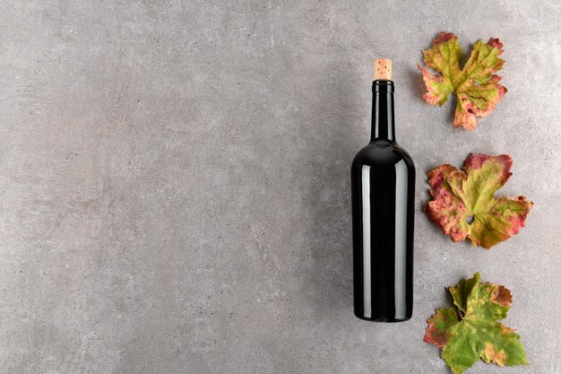 Red wine bottle fall grape's leaves on gray stone table