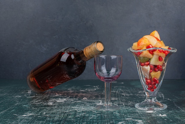 Бутылка красного вина, виноград и стакан смешанных фруктов на мраморном столе