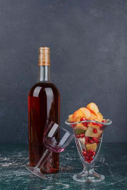 Bottiglia di vino rosso, uva e bicchiere di frutta mista sulla tavola di marmo.