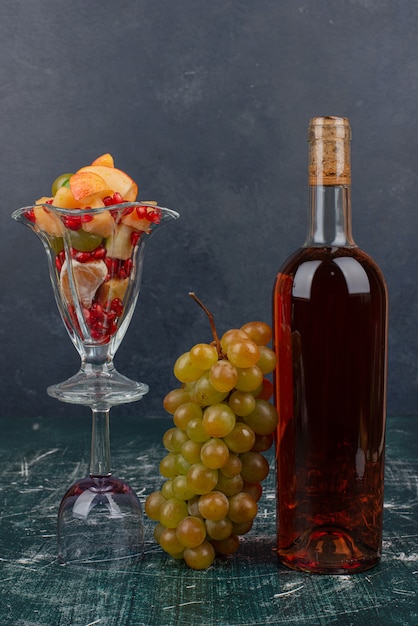 Red wine bottle, grapes and glass of mixed fruits on marble table.