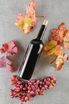 Red wine bottle with bunch of rose purple grape and fall grape's leaves, on gray stone table