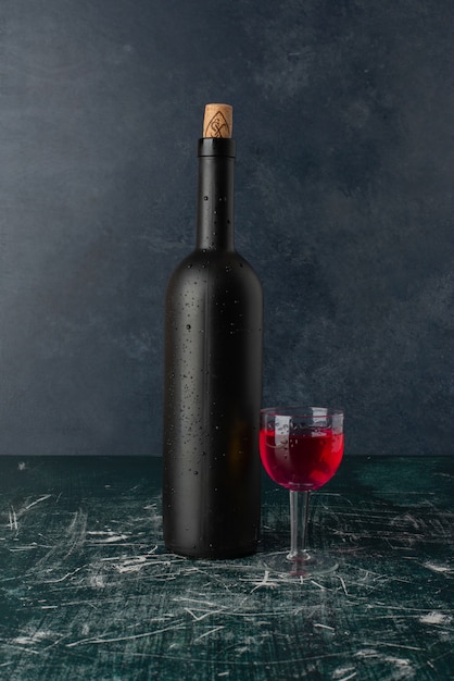 Red wine glass and bottle on marble table.