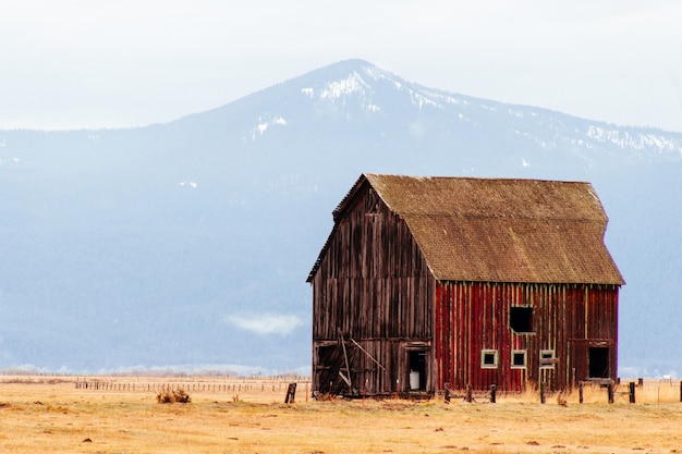Red wooden barn in a large field with mountains and hills