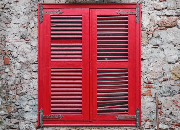 Red wooden blinds close the window on the old stone wall of the house Old brick wall idea for interior or loft studio and courtyard