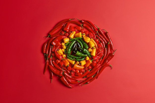 Red yellow and green pepper arranged in circle on red background. Colorful fresh vegetables. High angle view. Creative layout. Piquant seasoned hot chili. Vegetarian diet concept. Big variety