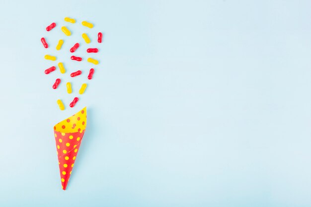 Red and yellow marmalade candies over the paper cone on blue background