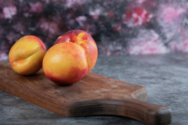 Red and yellow peaches on wooden board on table.