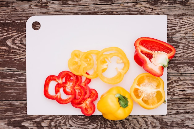 Red and yellow slices of bell pepper on white chopping board over the wooden desk