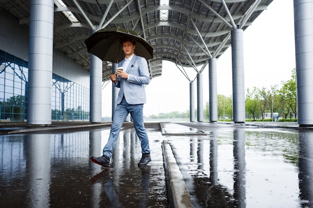 Foto gratuita uomo d'affari dai capelli rossi con ombrello bere caffè