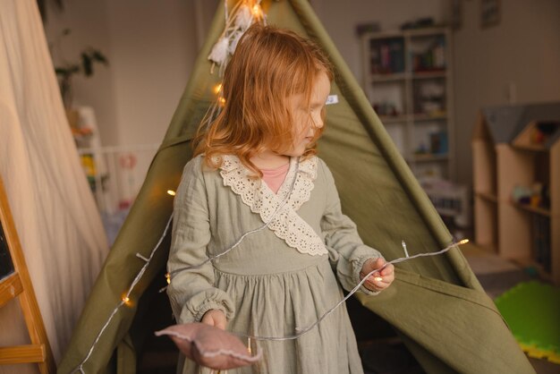 Redhaired little caucasian child in dress spends time in her room with toys Baby girl concept