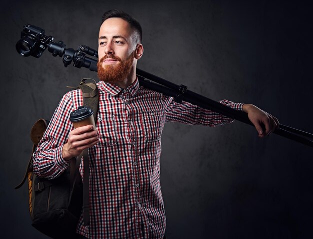 Redhead bearded freelance photographer with tripod and backpack.