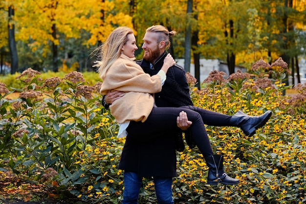 Redhead bearded male holds in his arms cute blonde female in an autumn park.