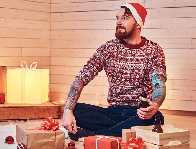 Redhead bearded male in Santa hat in a room with Christmas decoration.