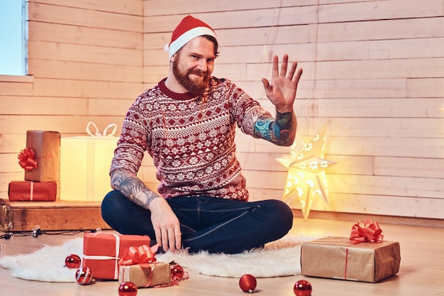 Redhead bearded male in Santa hat in a room with Christmas decoration.